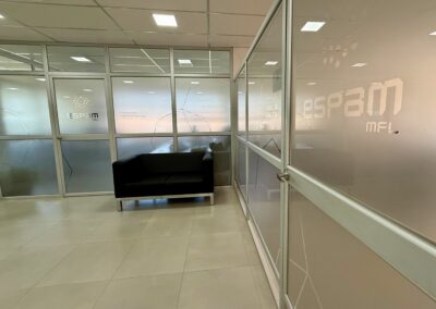 Recepción y pasillo de oficinas ESPAM MFL con mamparas de vidrio decoradas con vinil esmerilado institucional.